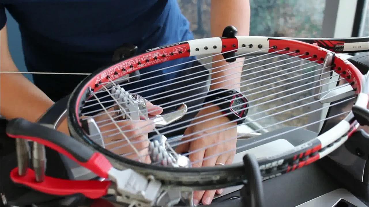A close-up of a tennis racquet on a stringing machine, showing the detail of a hybrid string setup.